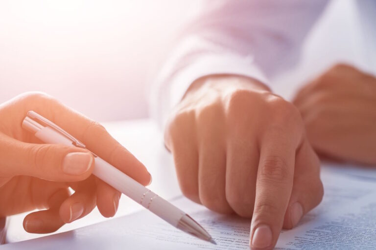 Close-up of hands signing a document with a white pen on a printed page
